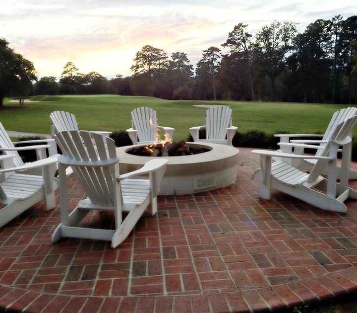 An outdoor brick patio with firepit and white outdoor chairs