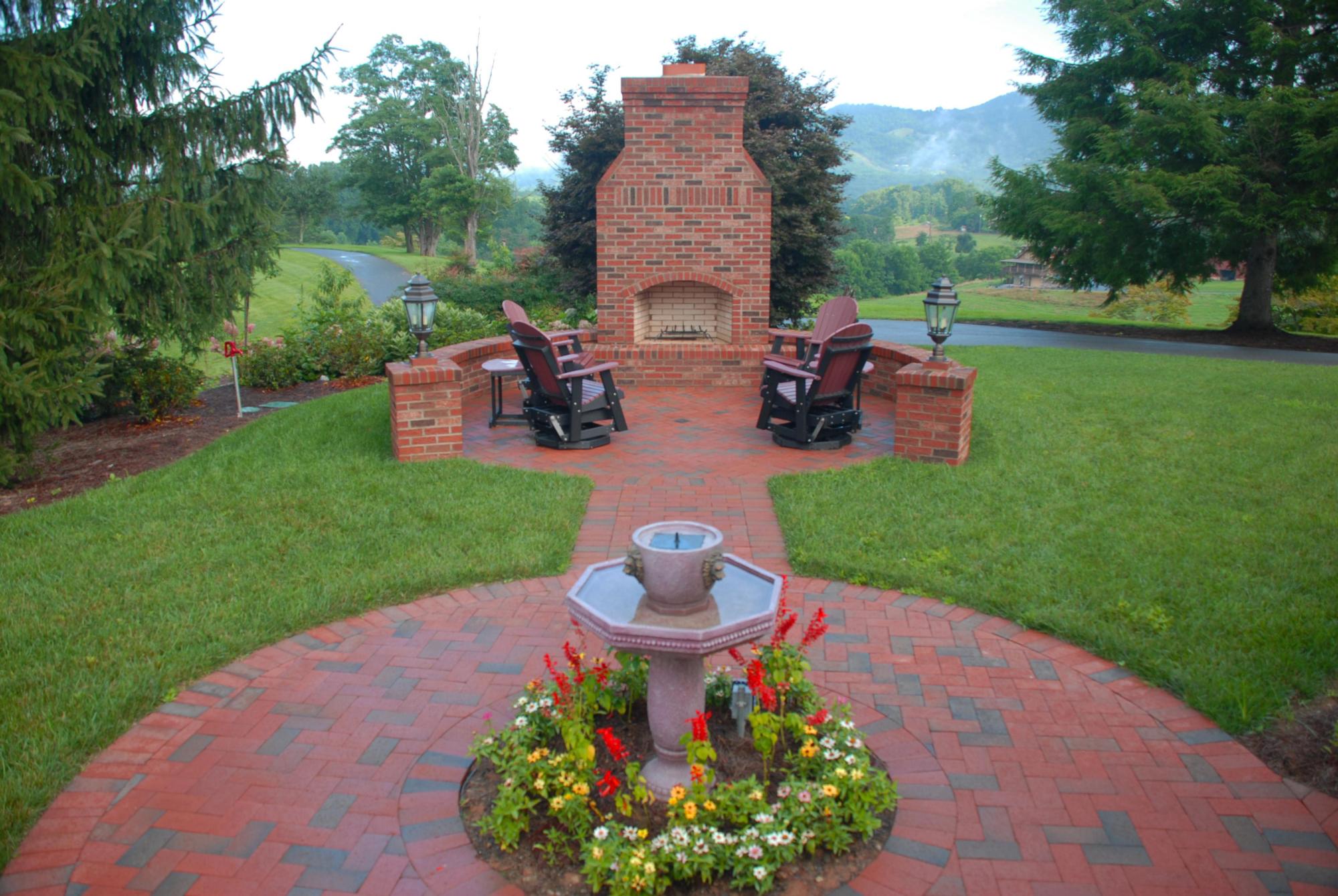 Image of a brick firepit and patio area with manicured lawn and flowers