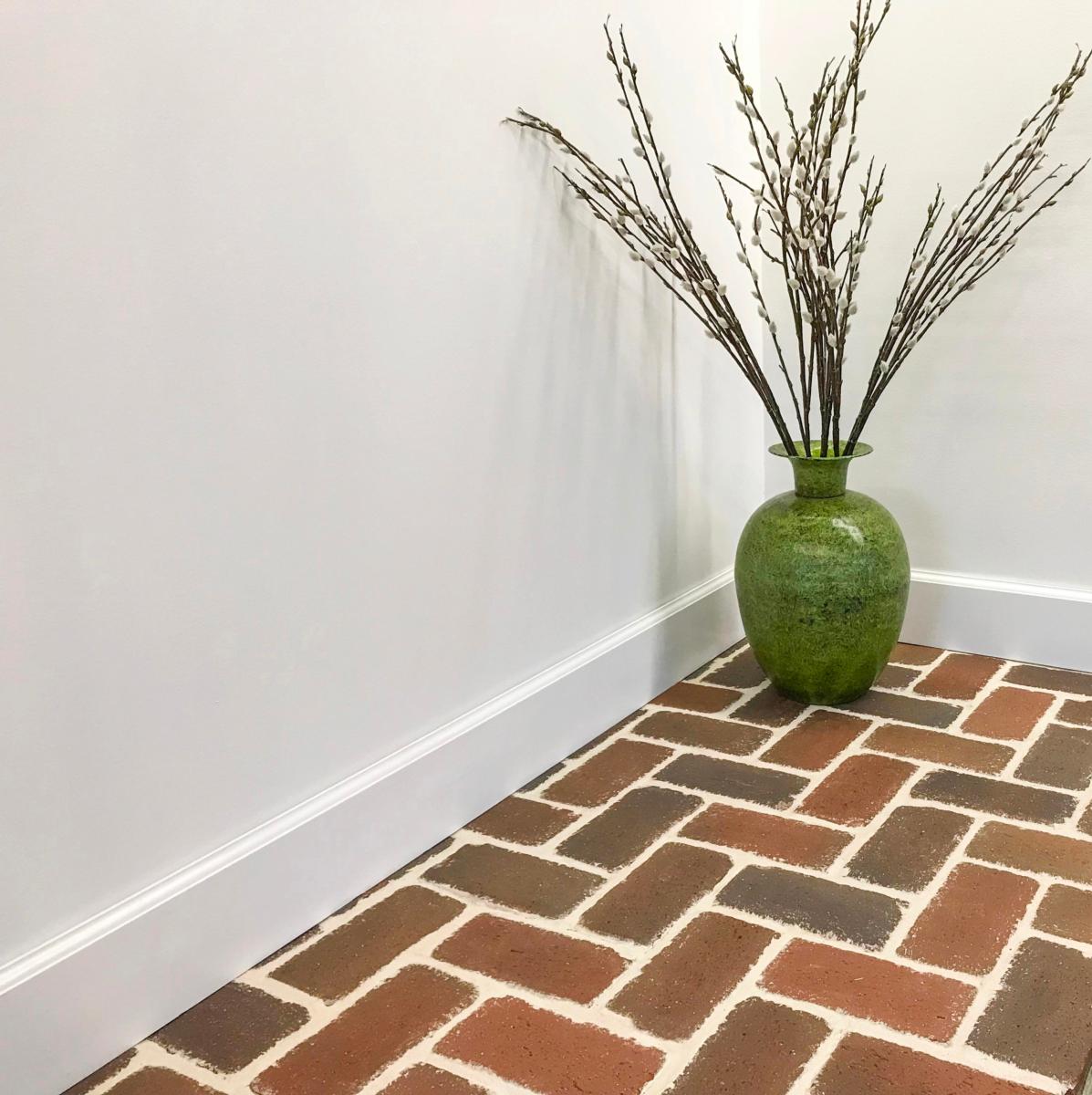 Image of a brick floor in an inside room with a decorative plant in the corner and white walls