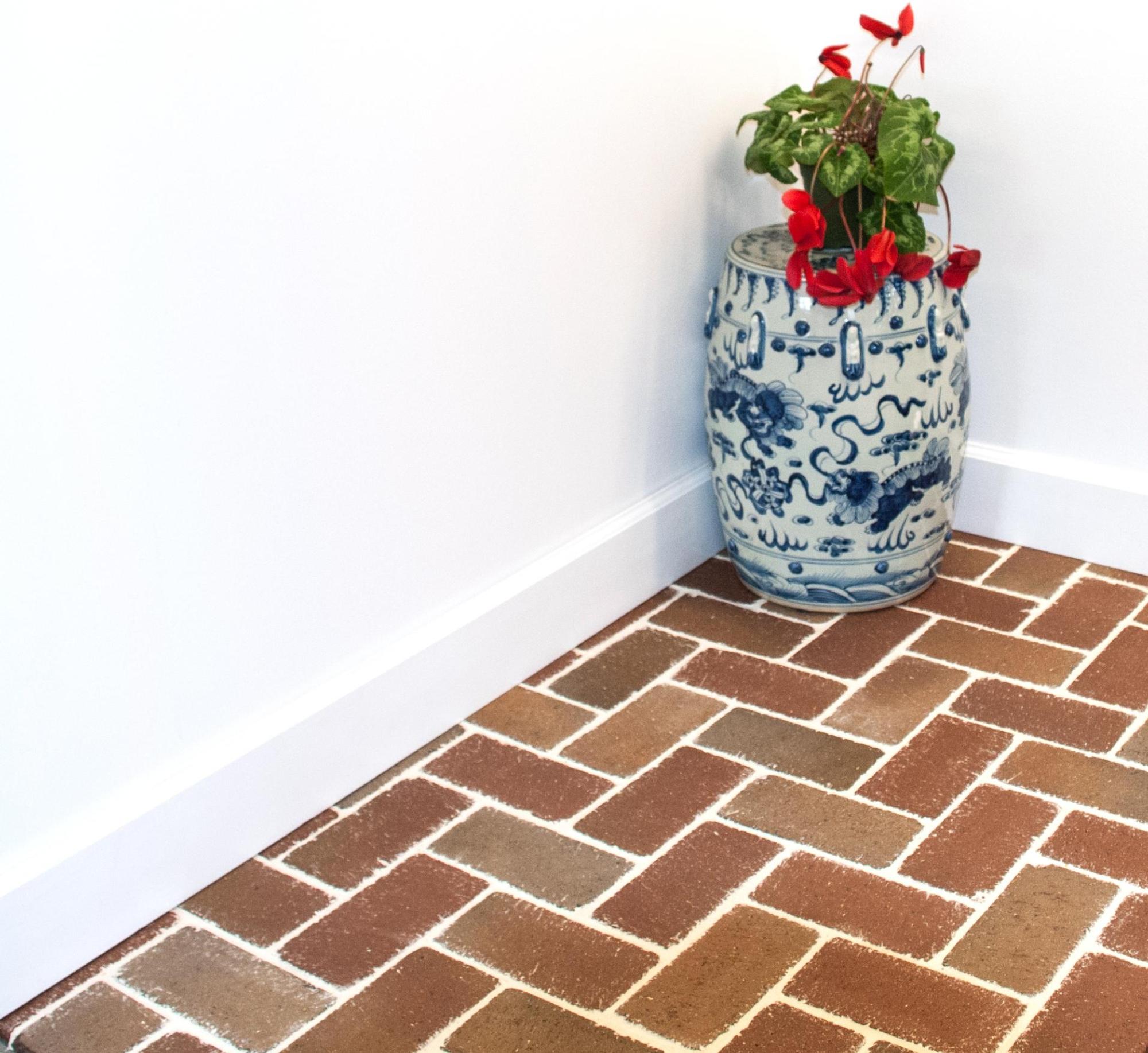 Image of a brick floor in an inside room with a decorative plant in the corner and white walls