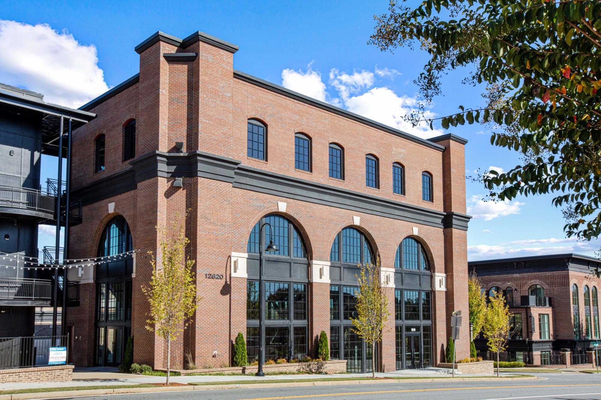 The Crabapple Marketplace, built of brick and surrounded by roads under a blue, partly cloudy sky.