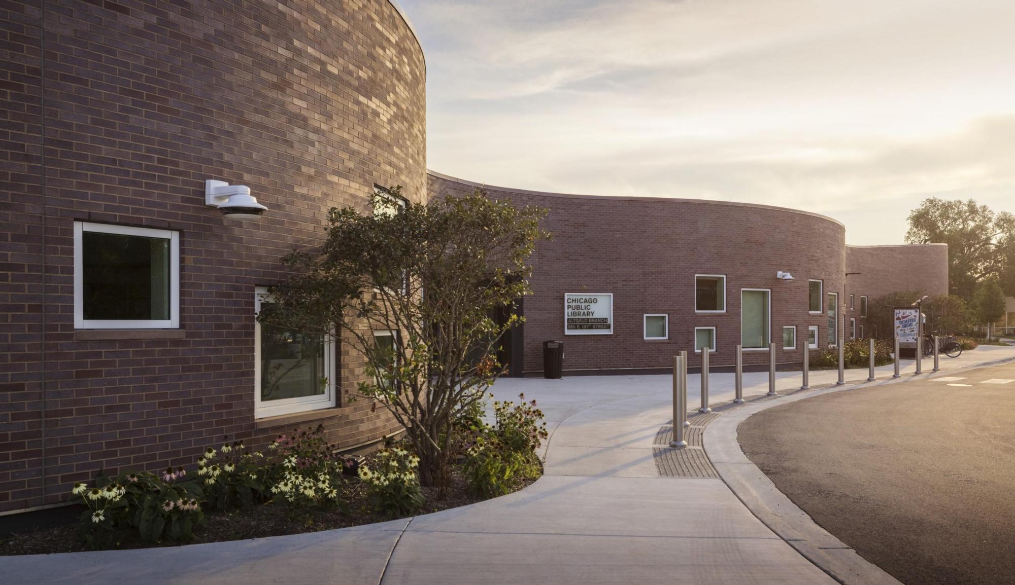 Altgeld Community Resource Center, illuminated by the morning sun, stands behind trees and bushes crafted of brown brick