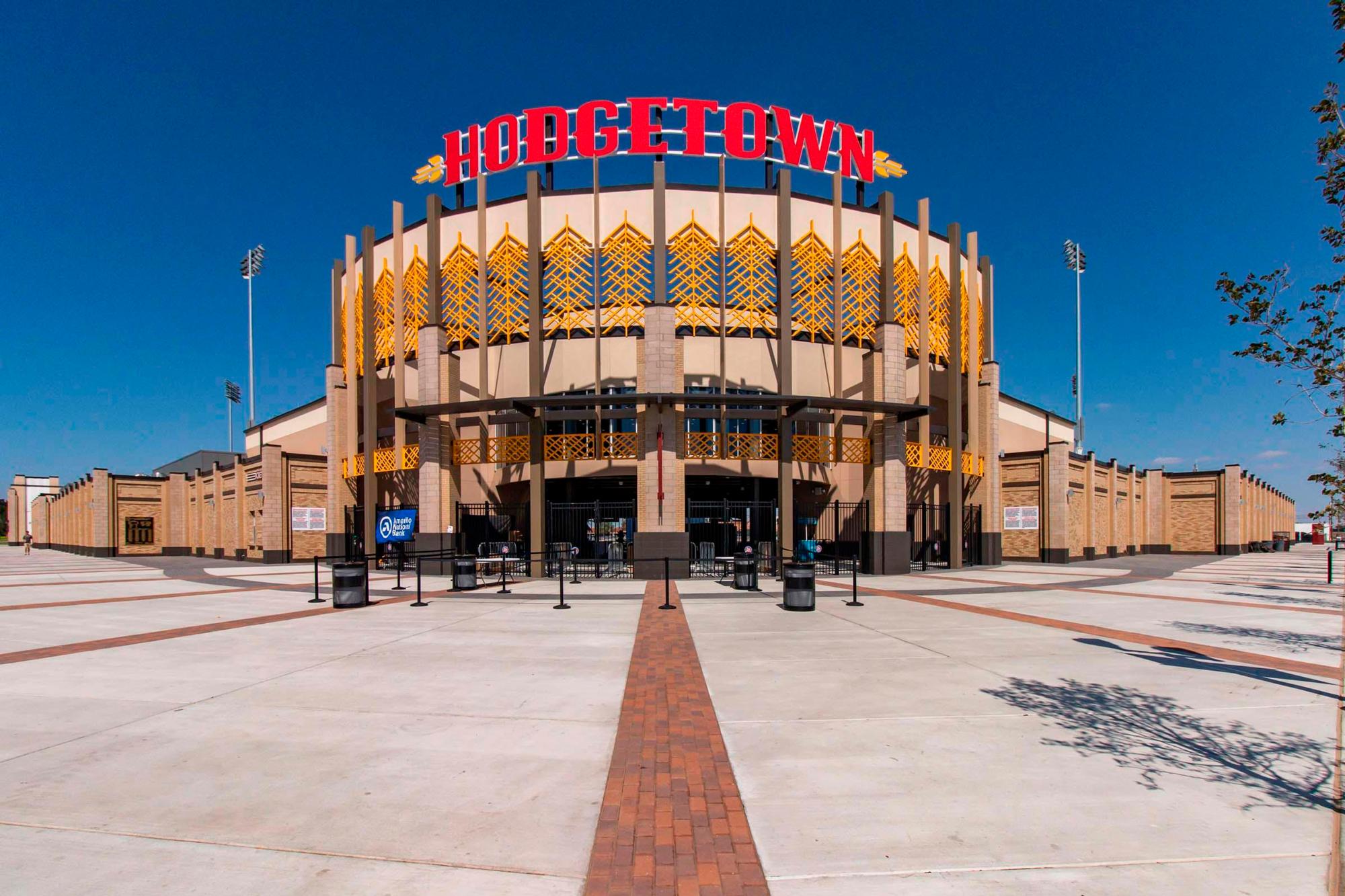 The exterior of Hodgetown; paved brick walkways lead to a coliseum style brick building with a sign atop: "Hodgetown"