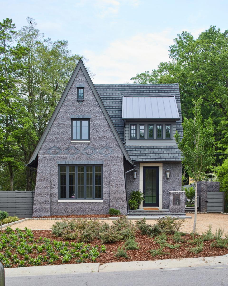 The trees and gray bricked exterior of the Neighborhood Cottage single-family home