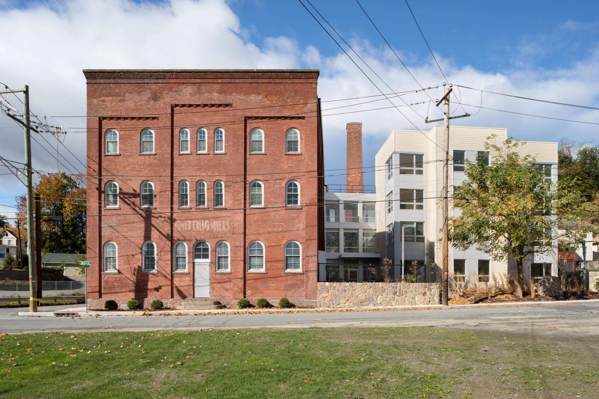 Exterior photo of The Mill at Middletown with green grass, concrete sidewalk, and the brown brick of the building