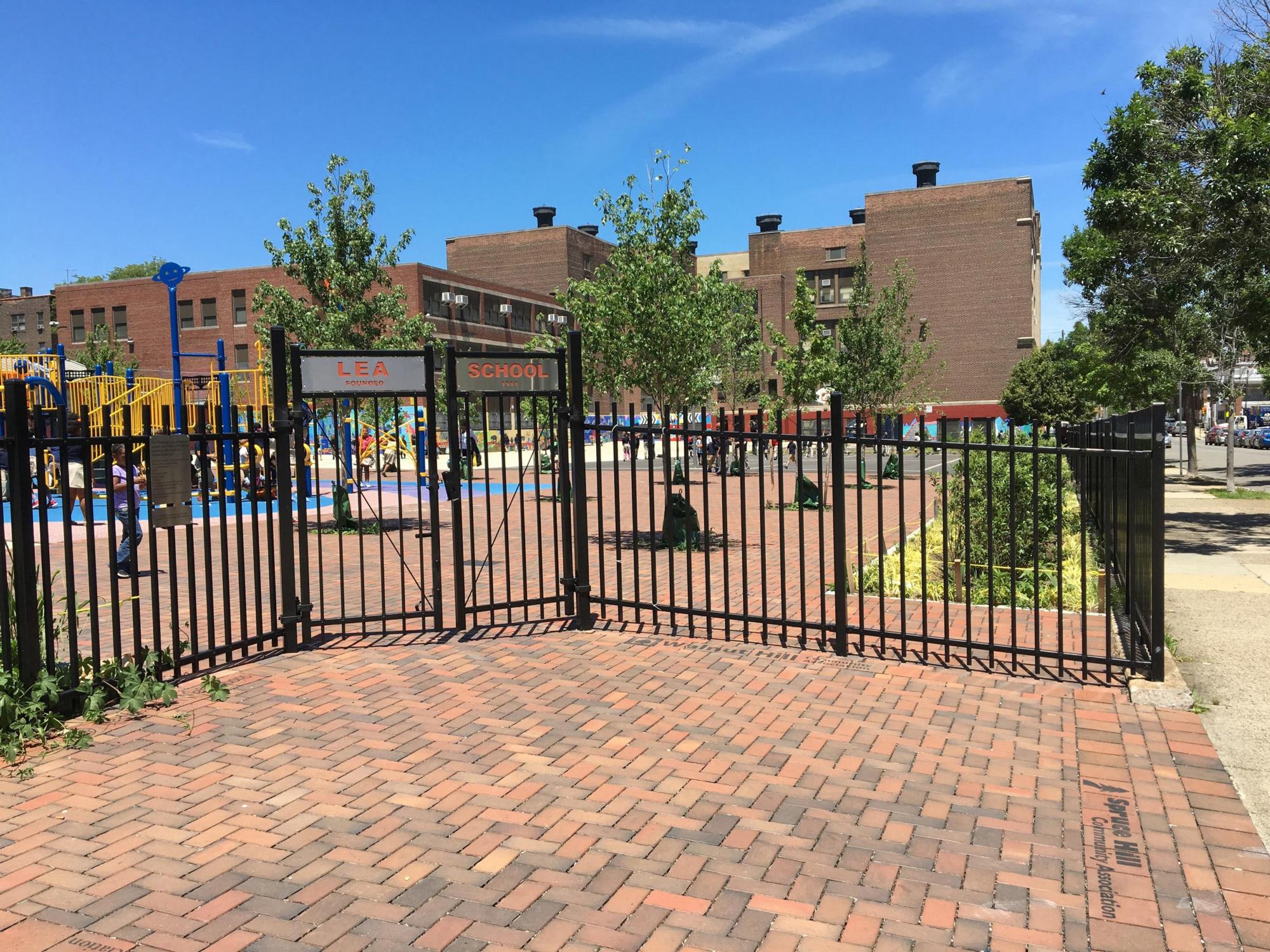 Brick walkway, metal fence, and shrubs of Lea Elementary