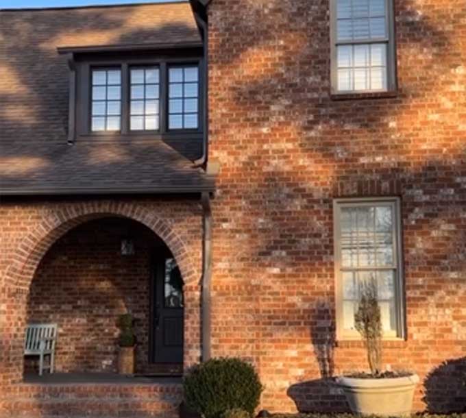 A brick farmhouse with shrubs in front of it